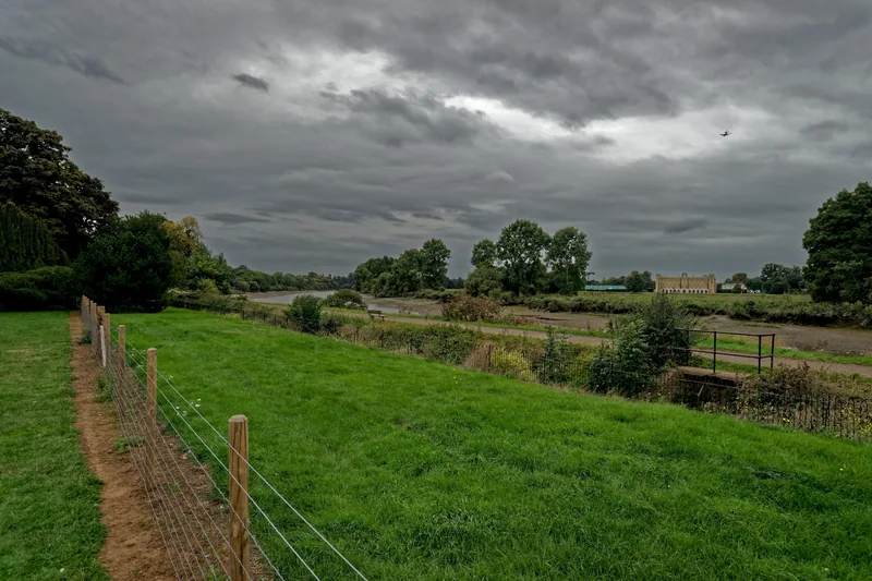 Syon House seen in the distance across the tidal Thames meadows from Kew under grey cloud