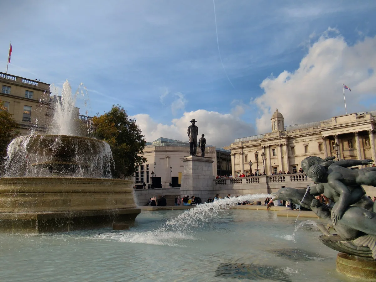 The fourth plinth in Trafalgar Square carrying two bronze figures, one in a wide-brimmed hat, a fountain playing in front of it