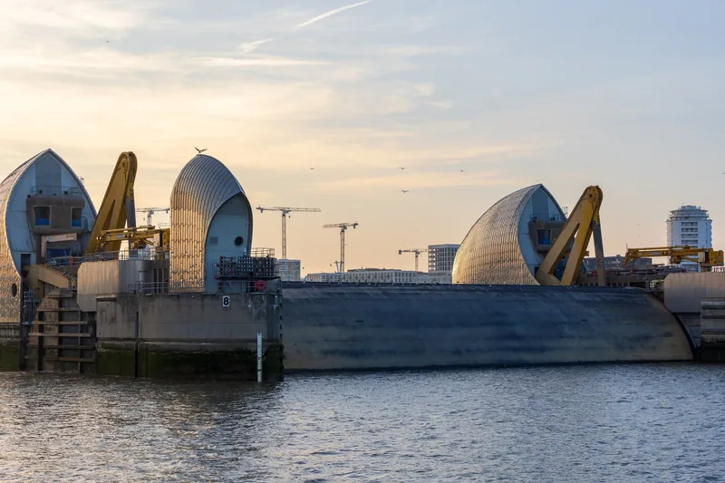 One gate of the Thames Barrier raised out of the water between its piers, seen from the south bank