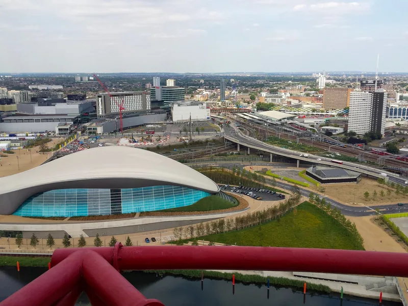 View from the ArcelorMittal Orbit over red steelwork to the London Aquatics Centre and Stratford beyond