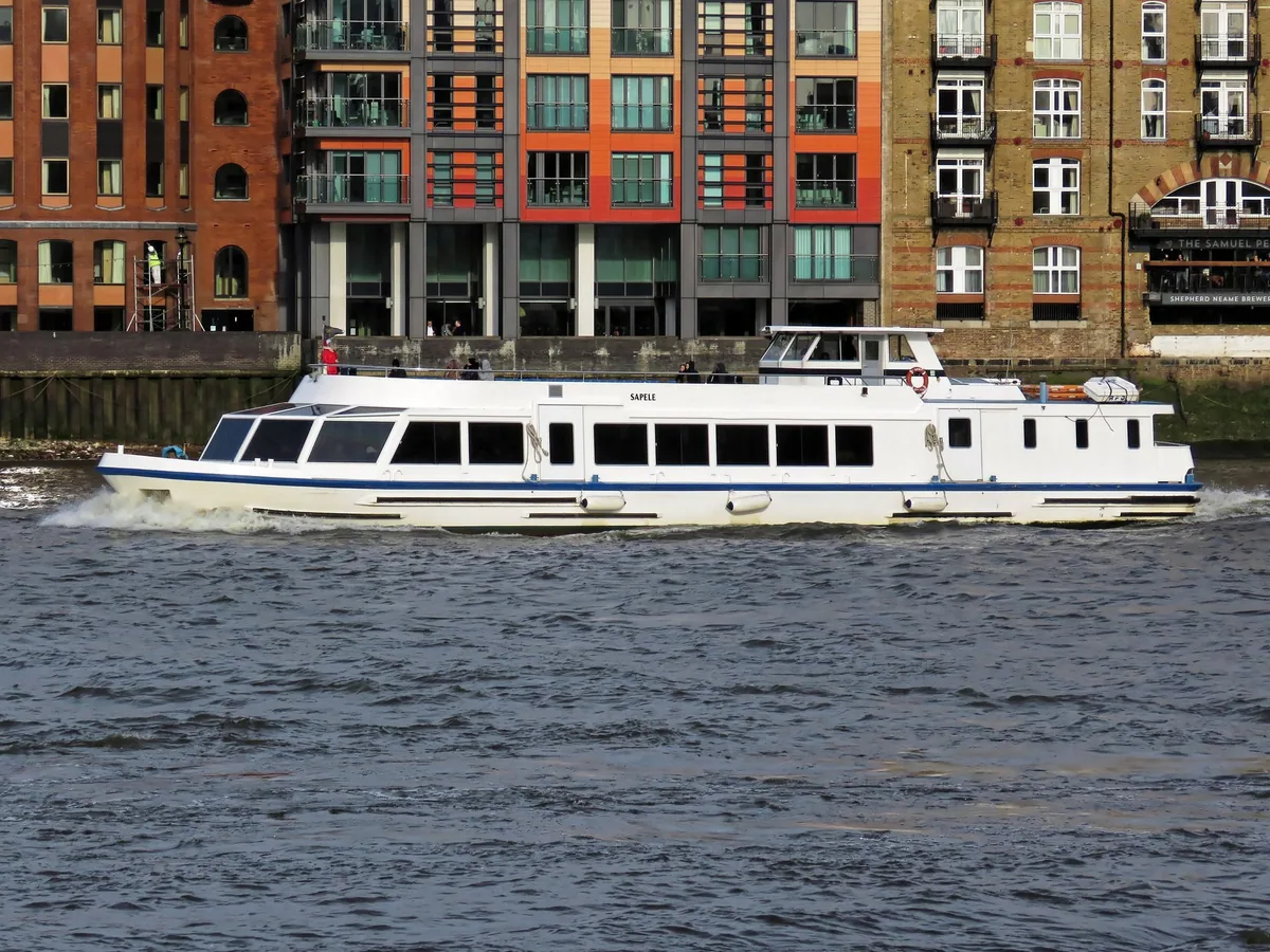White river cruise boat under way on the Thames past converted brick riverside warehouses