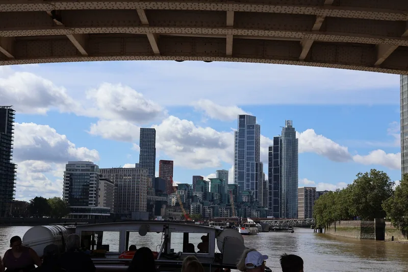 View from a Thames boat passing under a bridge girder towards riverside towers