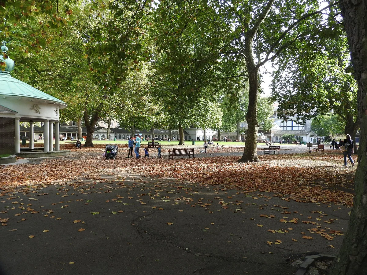 Plane trees and fallen leaves across the open ground at Coram's Fields, colonnade behind