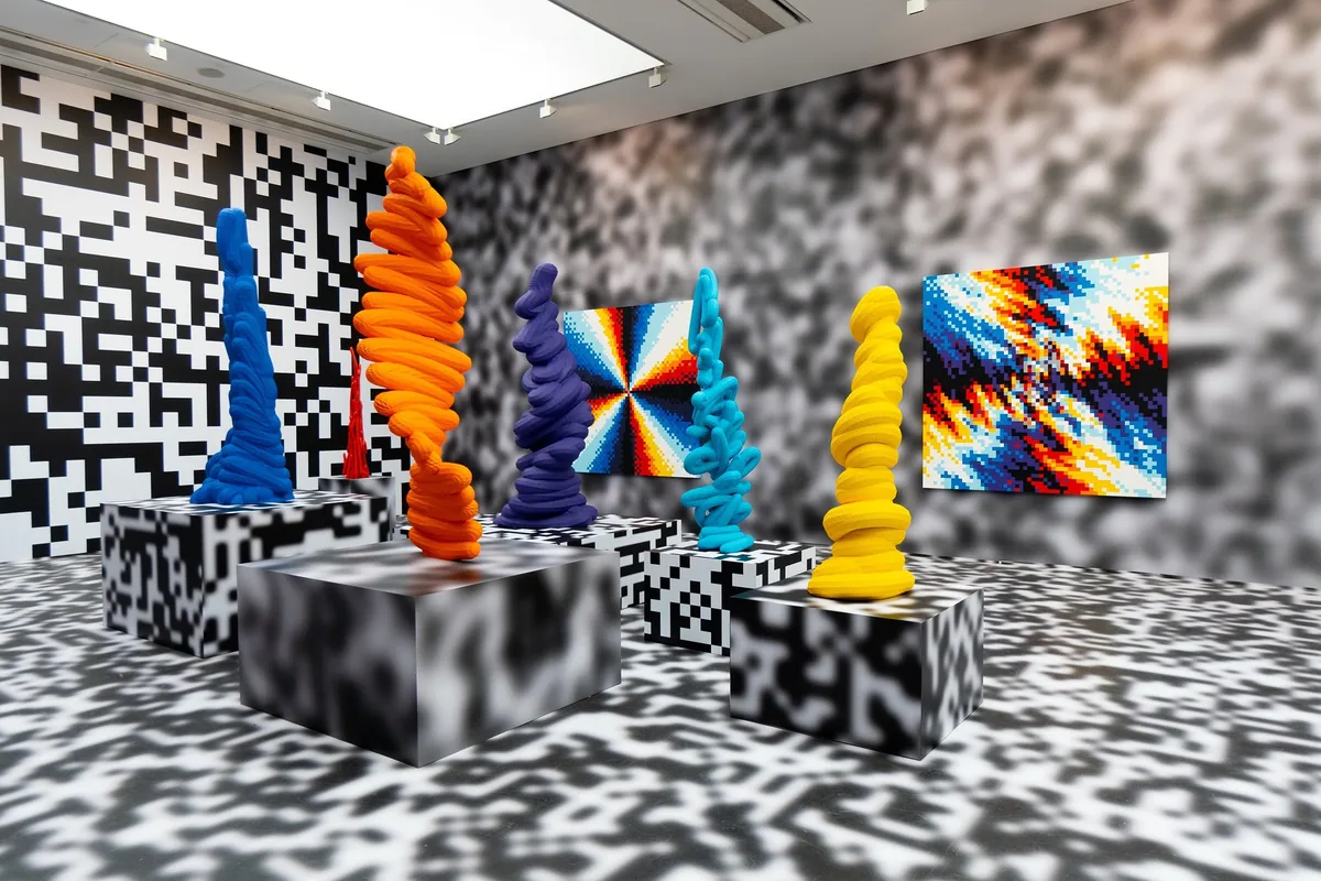 Gallery room where walls, floor and plinths are covered in pixel patterns around bright sculptures