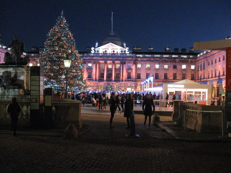 The floodlit courtyard of Somerset House at dusk, with a lit Christmas tree beside the seasonal ice rink