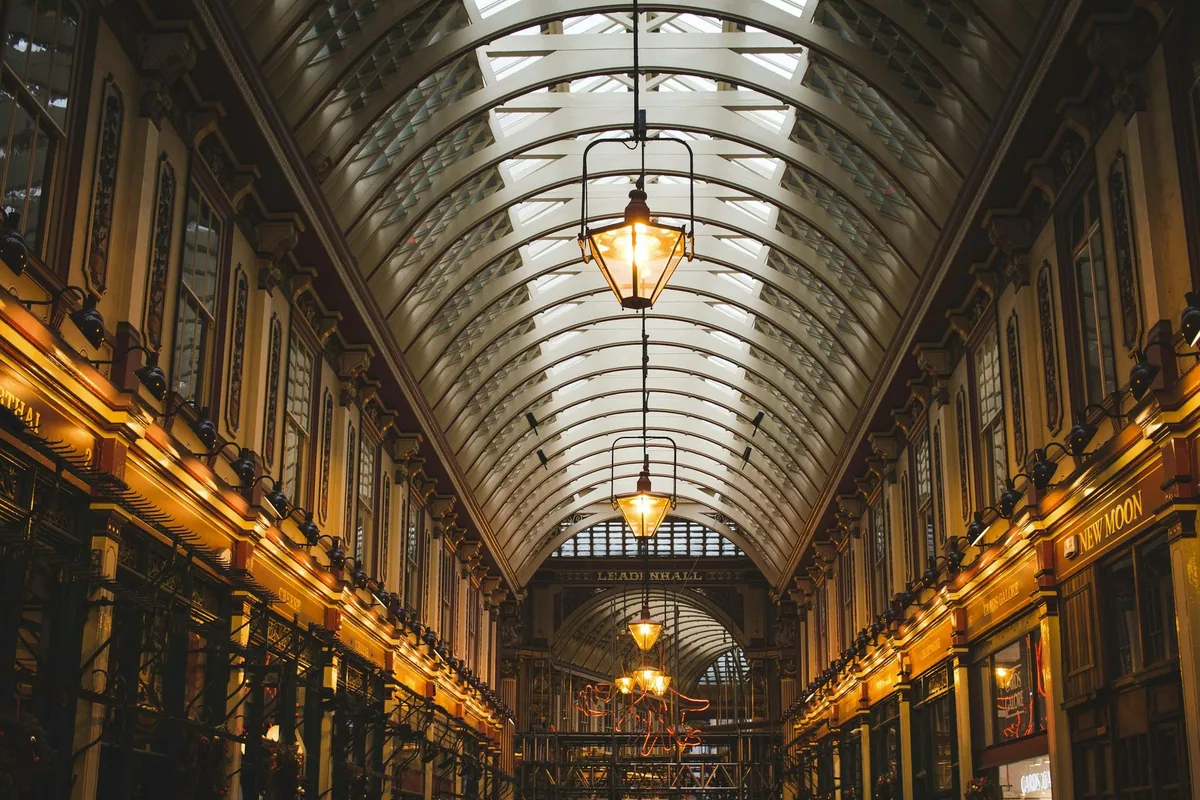 The glass-roofed Victorian arcade of Leadenhall Market after dark, lit by rows of hanging lanterns