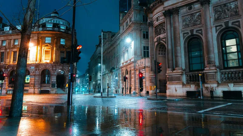 A rain-soaked street in central London at night, empty except for reflected lamplight and a traffic signal