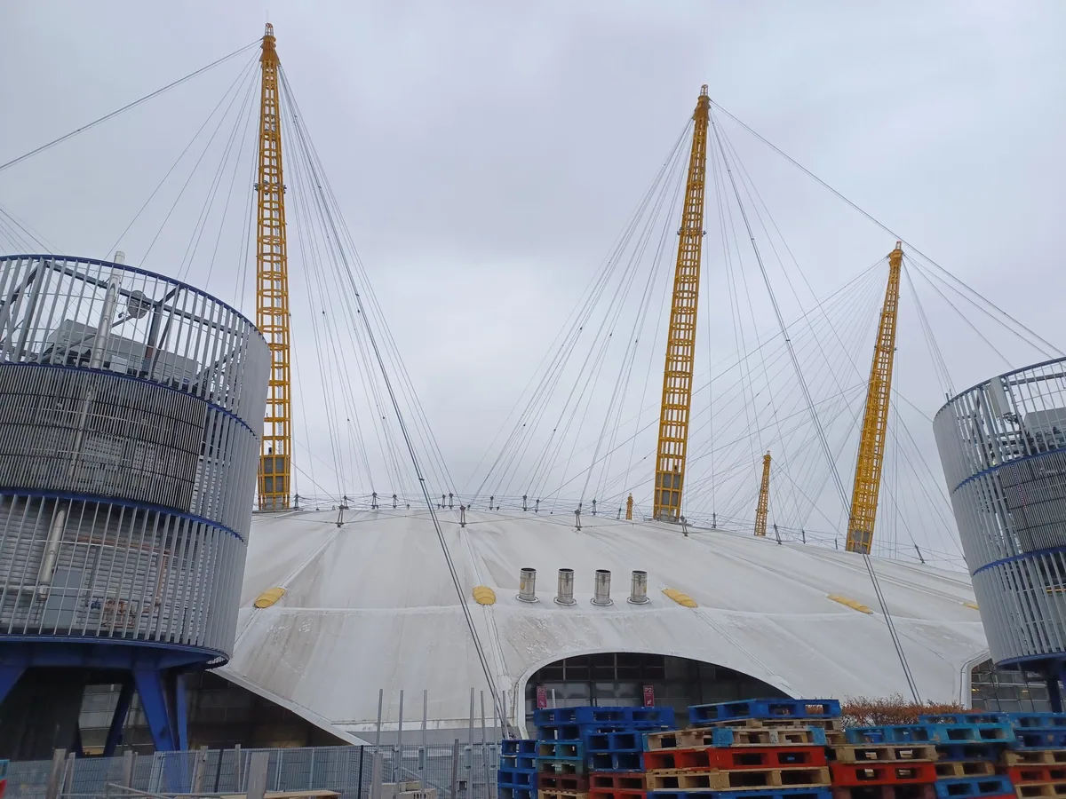 Yellow masts and white canopy of the O2 dome with tiny figures on the roof walkway