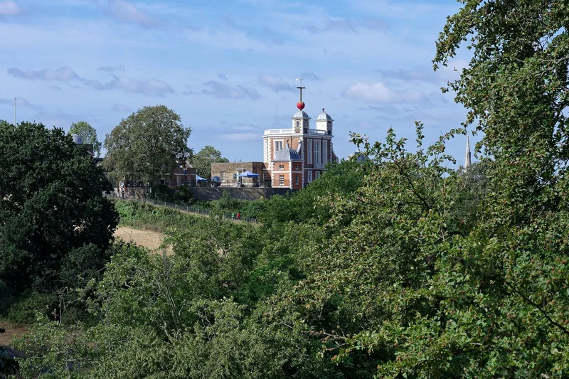 The Royal Observatory with its red time ball rising above summer trees, seen from One Tree Hill in Greenwich Park