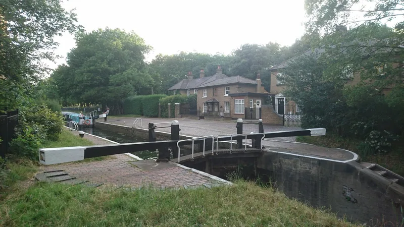 Top Lock on the Hertford Union Canal with its black and white balance beams closed across the chamber and a brick lock cottage behind