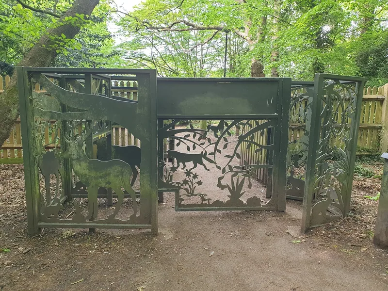 Decorative metal gate cut with deer and branches at an entrance to Highgate Wood