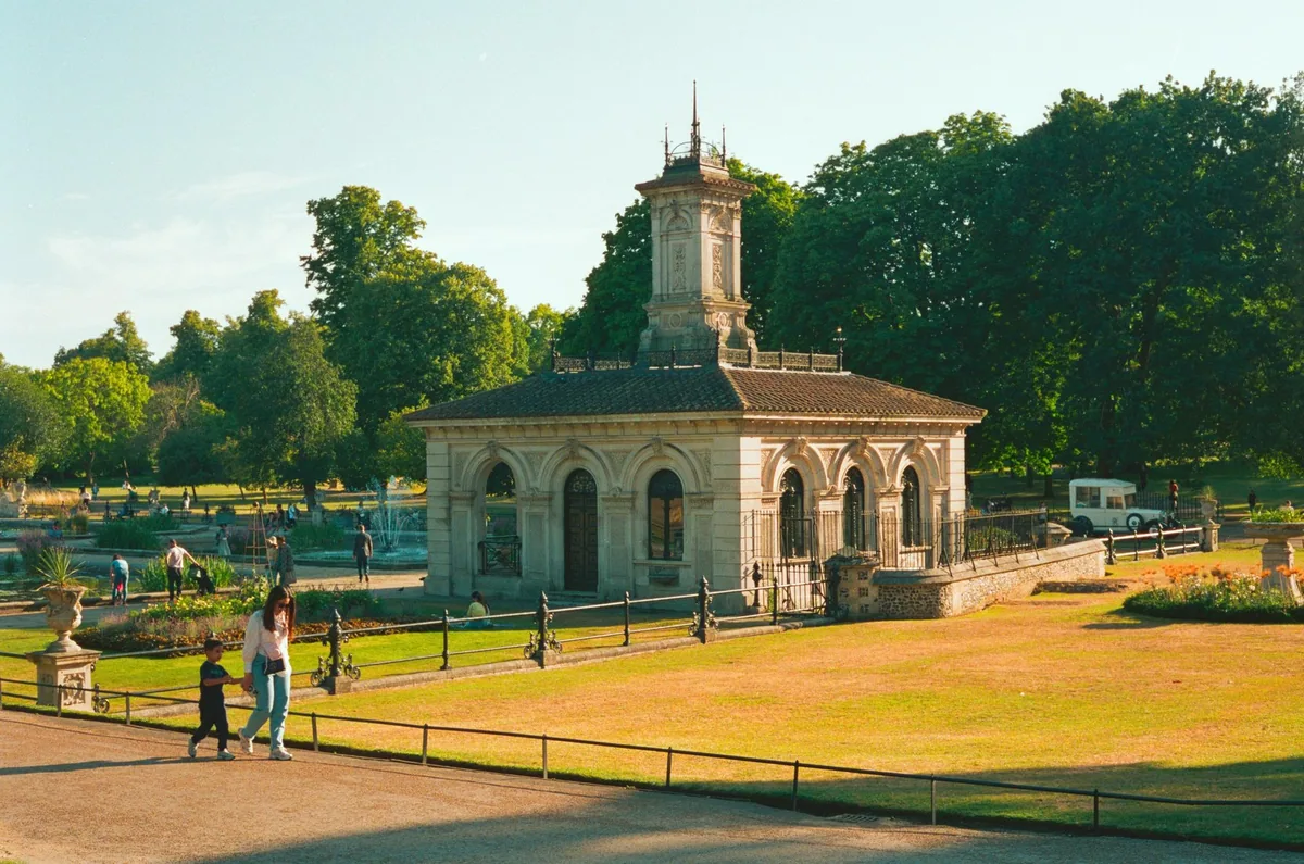 A historic stone pavilion in Hyde Park in golden evening light, with people walking on the path beside it