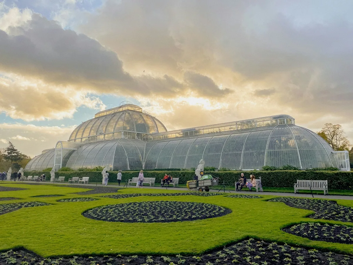 The curved glass roof of the Palm House at Kew Gardens behind its circular parterre beds in evening light