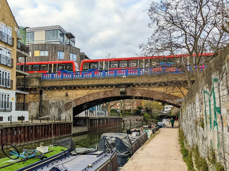 A Docklands Light Railway train crossing the brick viaduct over the Limehouse Cut, with moored narrowboats and the towpath below