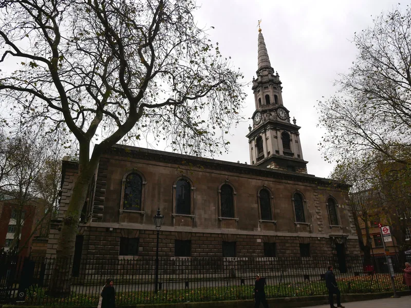 The north side of St Giles-in-the-Fields behind its railings, its stone spire and clock stage above bare plane trees