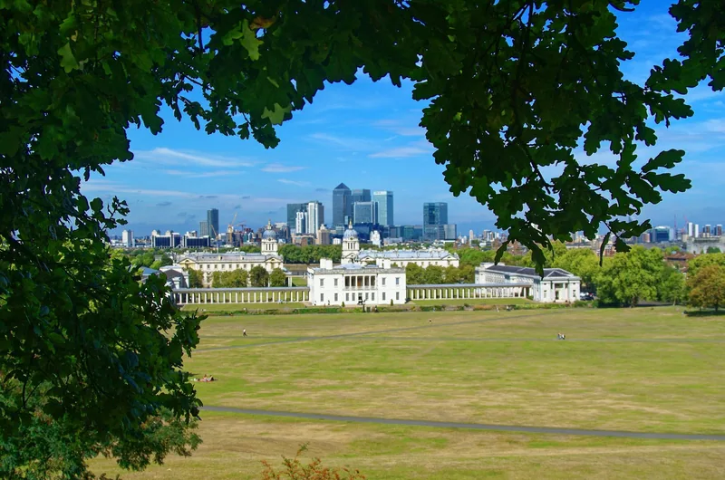 The Queen's House and the colonnades of the Old Royal Naval College below Greenwich Park, Canary Wharf behind, framed by oak leaves