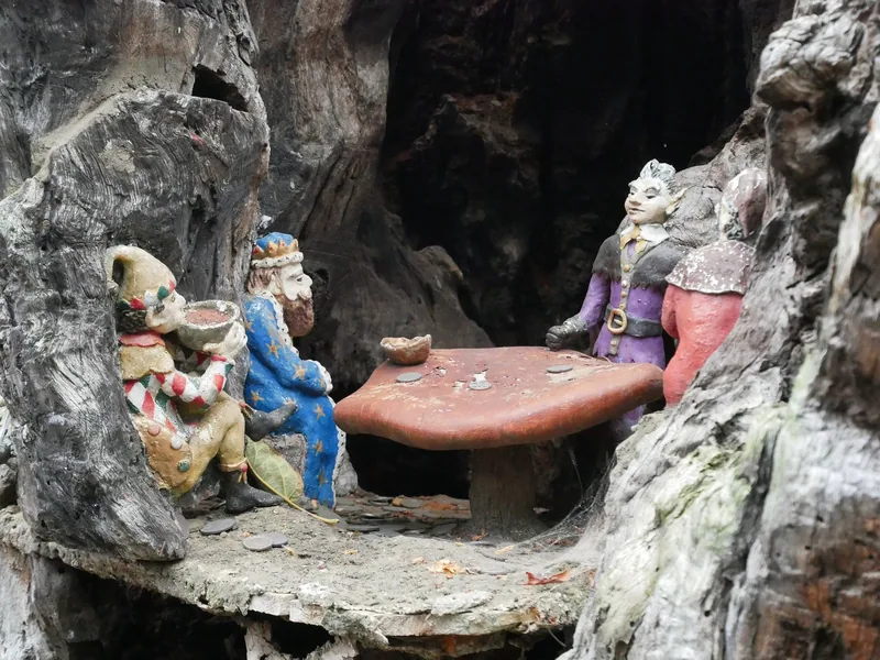 Painted elf figures carved into the hollow trunk of the Elfin Oak in Kensington Gardens, gathered round a toadstool table