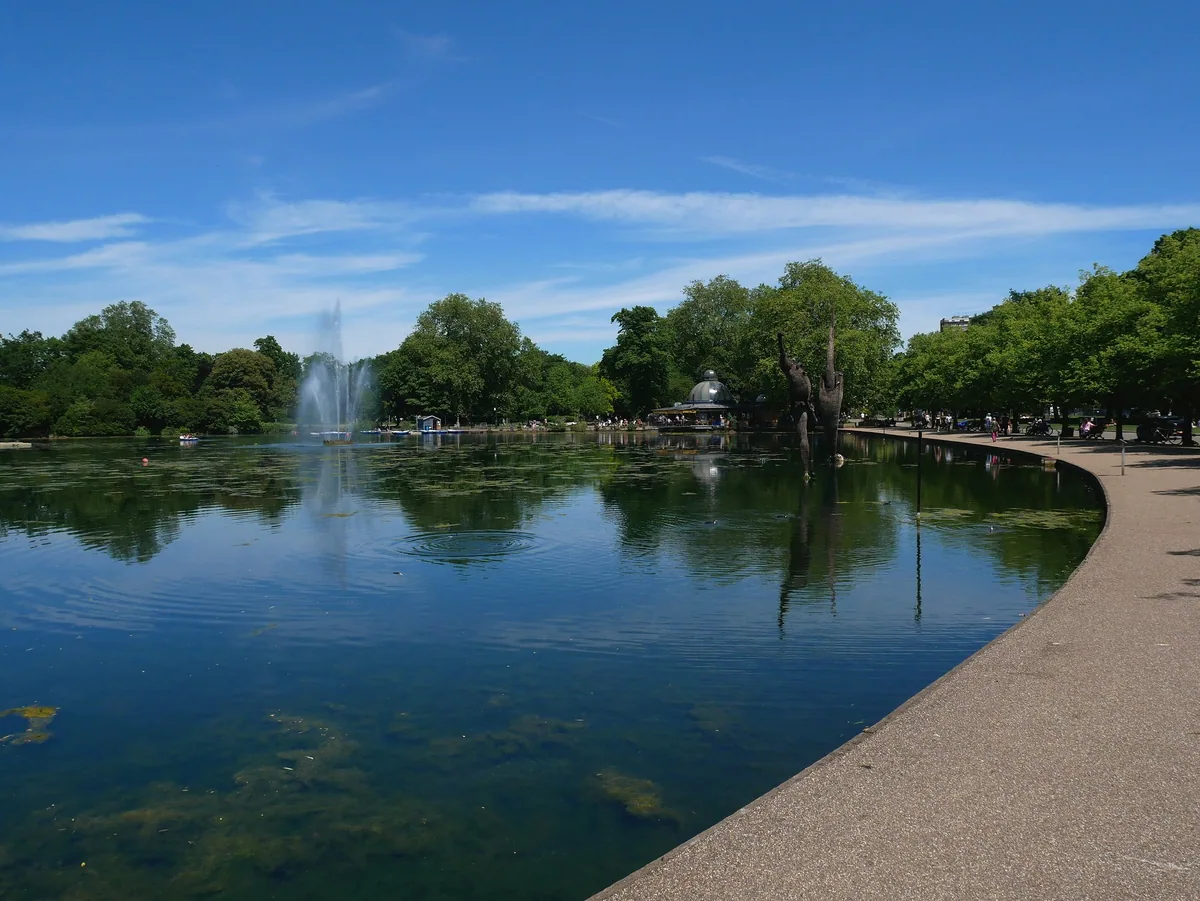 Fountain jet playing on the West Boating Lake in Victoria Park, with the wide tarmac path curving along the water