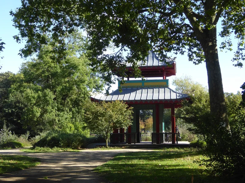 The red and green Chinese pagoda on its island in Victoria Park, reflected in the still water of the boating lake