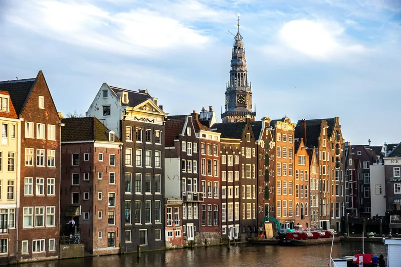 Leaning gabled canal houses in central Amsterdam with a church tower rising behind