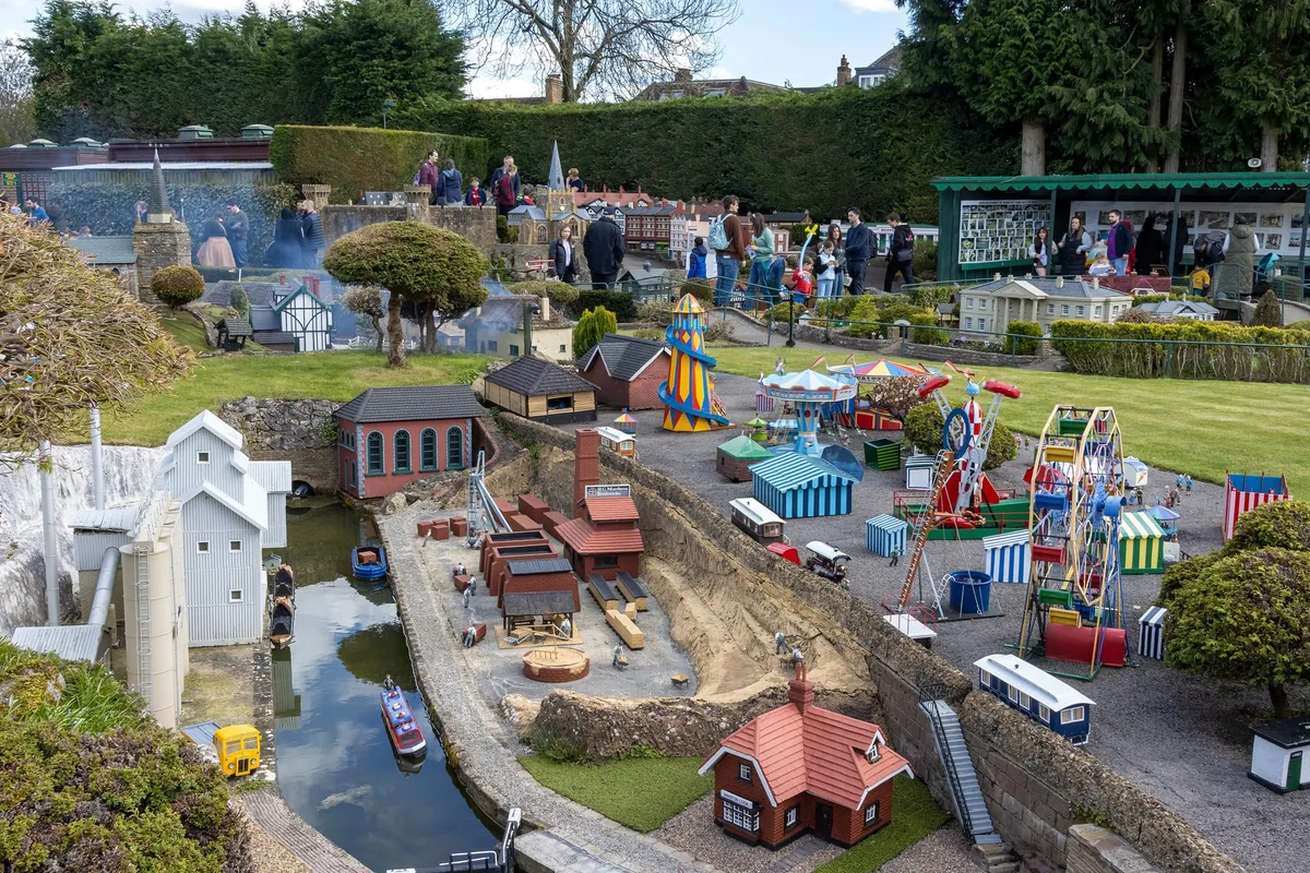 The miniature fairground at Bekonscot model village, with a big wheel, a carousel and striped stalls beside a model canal and wharf