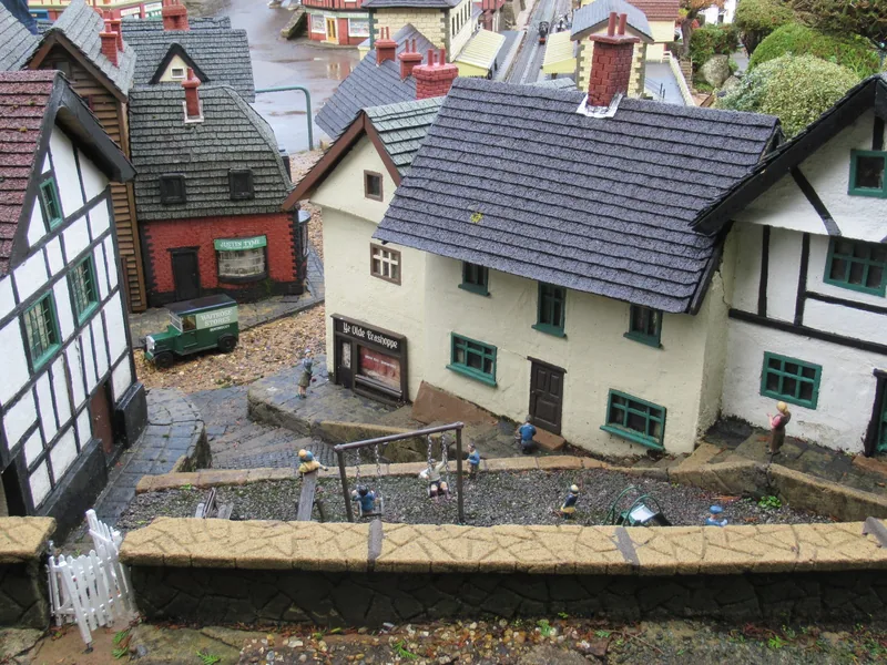 Close view of model cottages at Bekonscot, a tiny delivery van in a cobbled lane and painted figures around a miniature swing