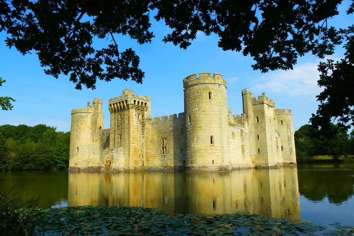 Bodiam Castle's round corner towers and battlemented curtain wall rising straight out of the moat, mirrored in the still water