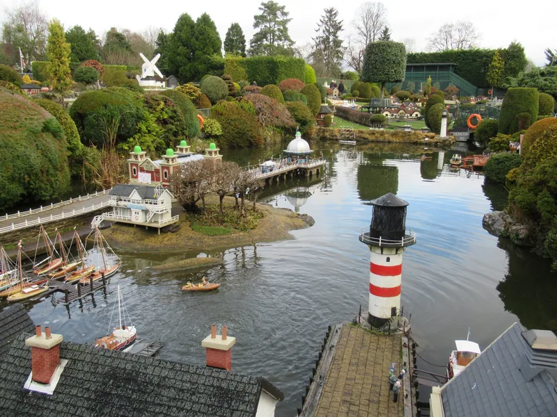 The model lake at Bekonscot, with a red and white lighthouse, moored toy yachts and a miniature windmill on the hill