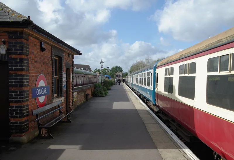 Ongar station platform with a red roundel nameboard on the brick building, a wooden bench, and a rake of carriages alongside