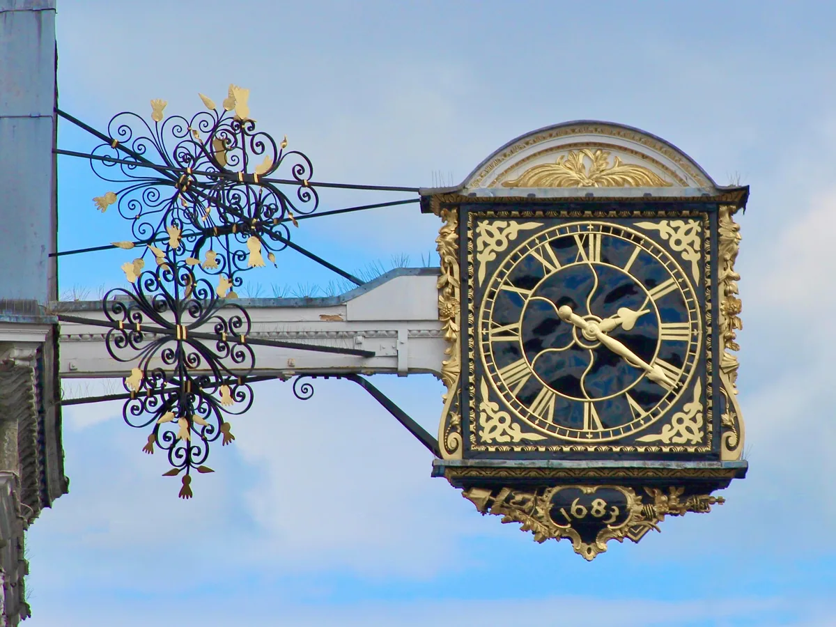The gilded Guildhall clock of 1683 projecting over Guildford High Street on its ornate iron bracket against a blue sky