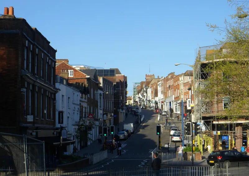 Guildford High Street climbing away between brick and painted shopfronts, with traffic lights and parked cars on the slope