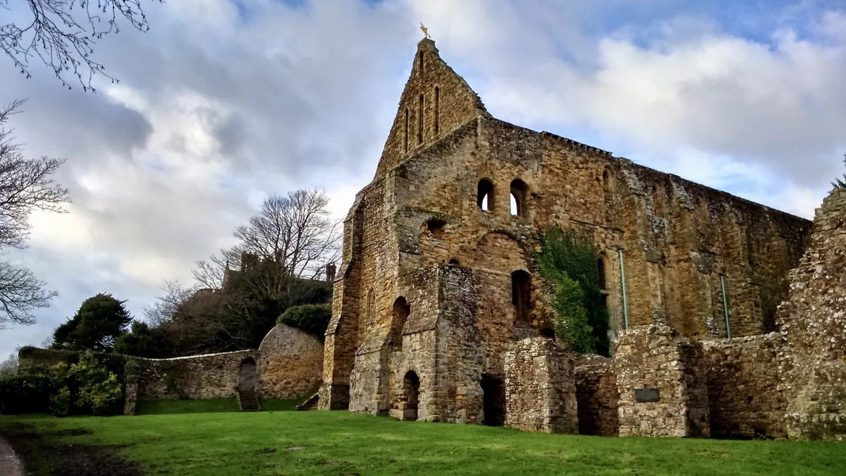 The ruined stone dormitory range of Battle Abbey standing above a green lawn