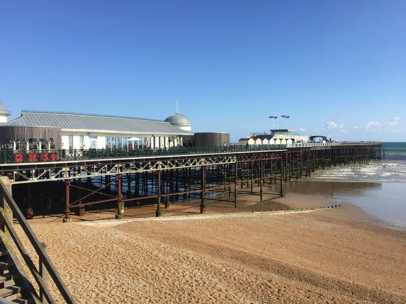 Hastings Pier stretching out over the shingle beach under a clear blue sky