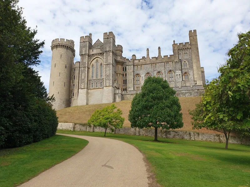 Arundel Castle in West Sussex rising above its grassy bank, seen along a curving drive through the park