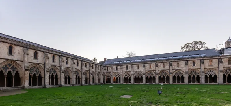 Two ranges of the stone cloister at Norwich Cathedral, their tracery arches running round a square of grass