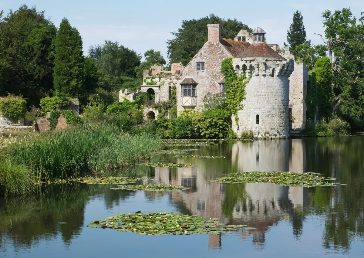 The moated ruin of Old Scotney Castle in Kent reflected in a lily-covered lake, with its round tower above the reeds