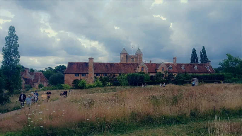 The long brick range and twin-turreted tower of Sissinghurst Castle seen across a rough meadow in Kent