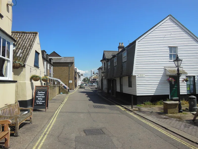 Narrow High Street in Old Leigh at Leigh-on-Sea, lined with white weatherboarded cottages and a pub bench