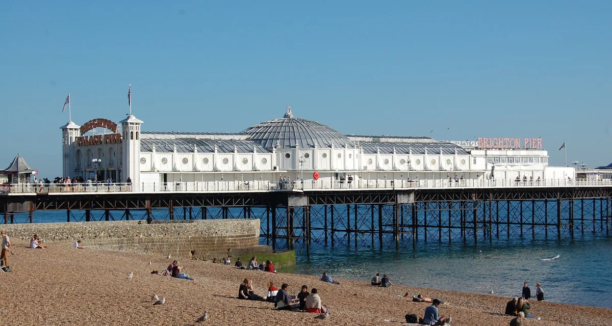Brighton Palace Pier and its white domed pavilion seen from the shingle beach, with people sitting in the sun