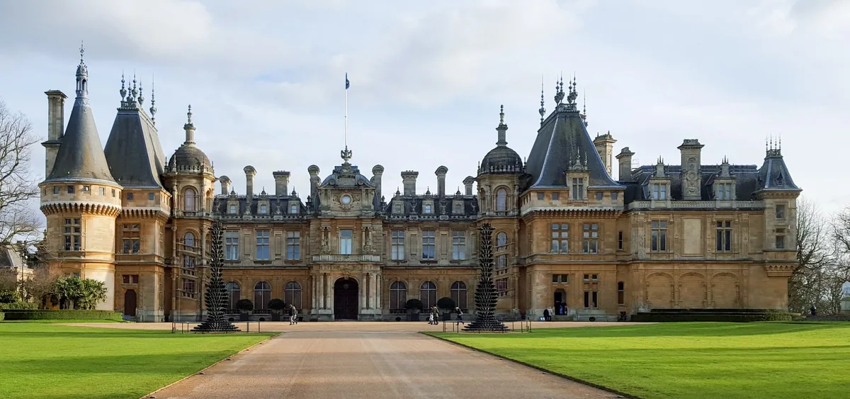 The symmetrical pale stone front of Waddesdon Manor with turrets and steep grey roofs, a gravel drive running straight to the door