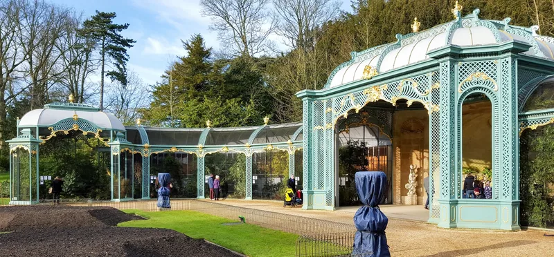 The curved wrought-iron aviary at Waddesdon, painted pale green and picked out in gold, with planted cages behind the mesh