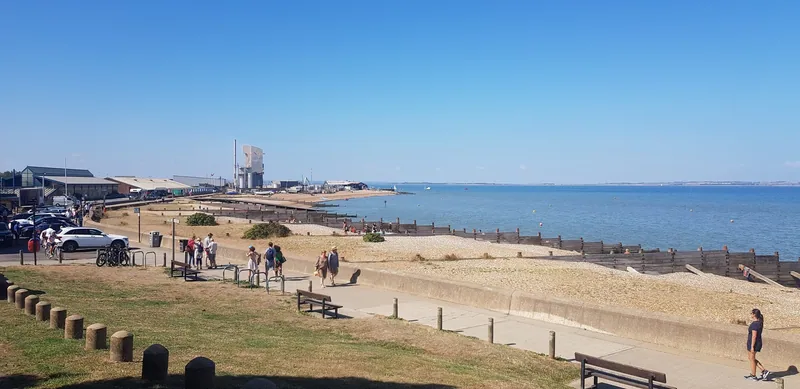 People walking on Whitstable's shingle beach on a clear summer day, with calm sea stretching to the horizon