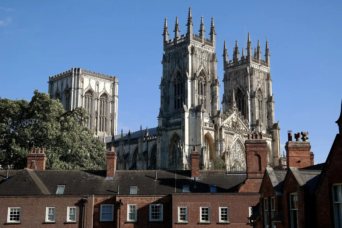 The towers of York Minster rising above brick rooftops and chimneys under a blue sky