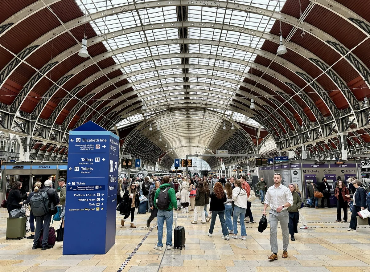 Travellers with suitcases crossing the concourse of Paddington station under its curved glass and iron roof