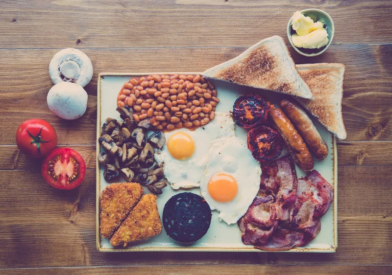A full English breakfast on a square plate: bacon, sausages, black pudding, beans, fried eggs, hash browns and toast