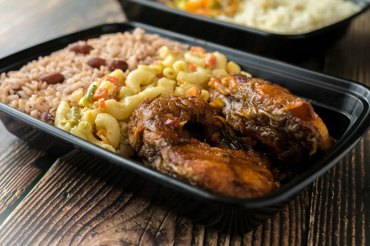 A takeaway tray of rice and peas with macaroni salad and pieces of brown-stew fish