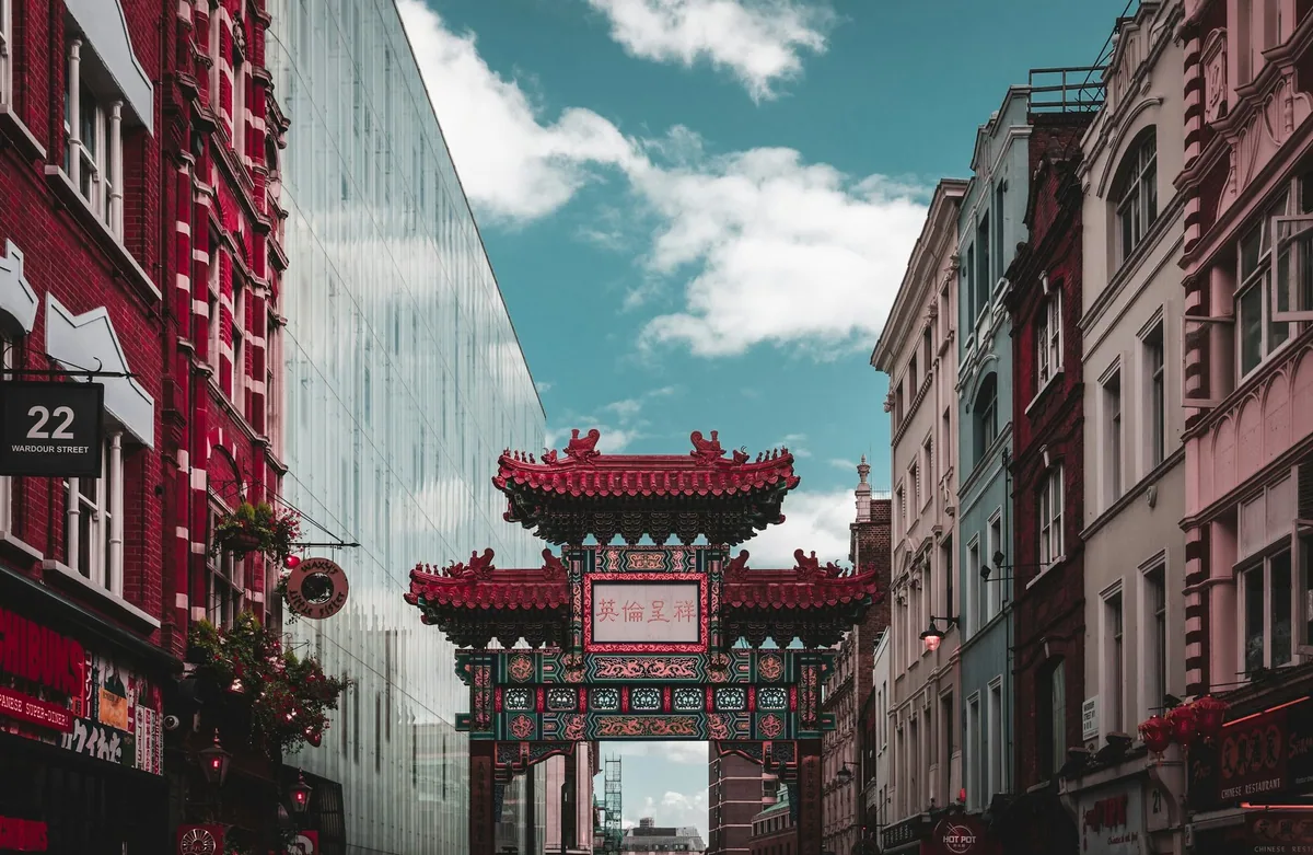 The ornate Chinatown gate standing between London townhouses under a blue sky with clouds