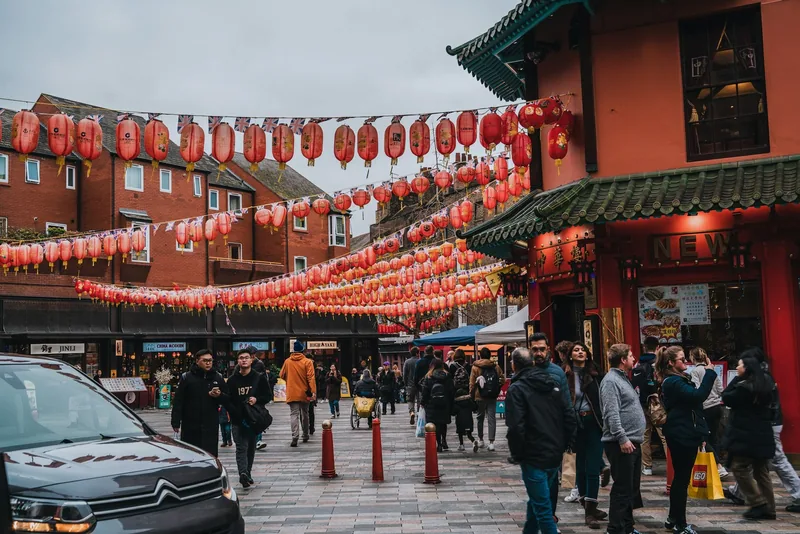 Rows of red lanterns strung above a busy Chinatown street with shoppers and restaurants