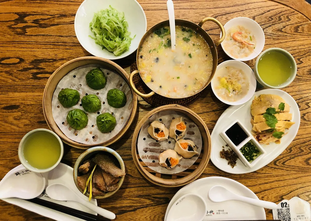 A wooden table spread with bamboo steamers of dim sum, small dishes and cups of green tea, seen from above