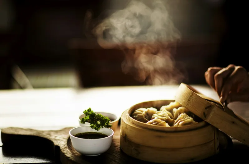 Steam rising from a bamboo basket of freshly cooked dumplings served with a dipping bowl